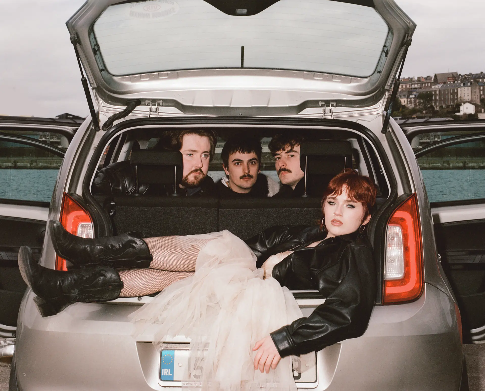 band posing in the boot of a silver car